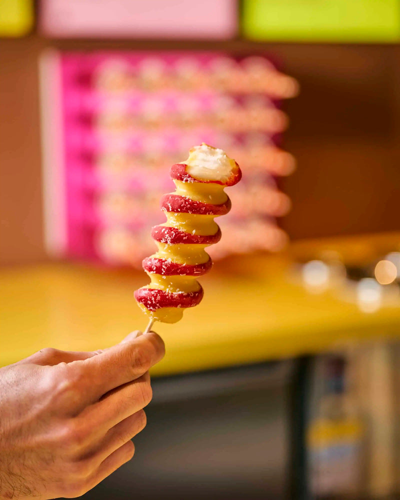 Hand holding a spiral skewer of red strawberries with yellow glaze and sprinkles at GLO Pasticceria
