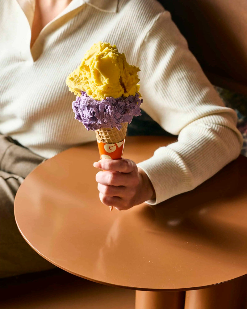 Person holding a double-scoop yellow and purple gelato cone at GLO Pasticceria