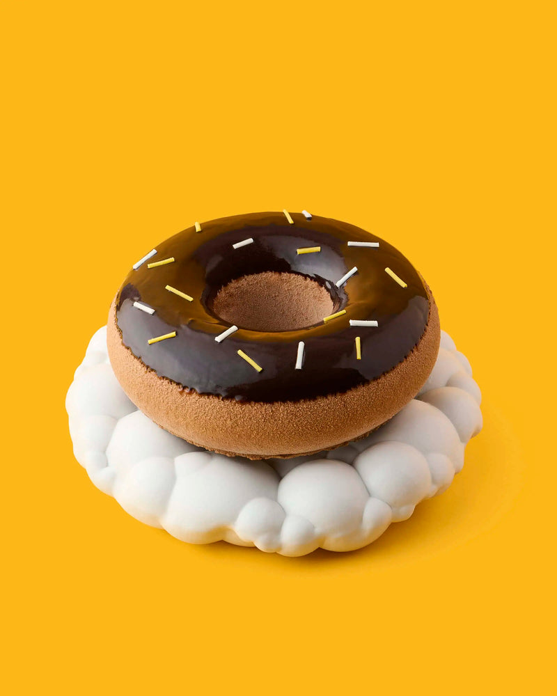 Chocolate glazed ring pastry with sprinkles on a white cloud-shaped stand against a yellow background at GLO Pasticceria