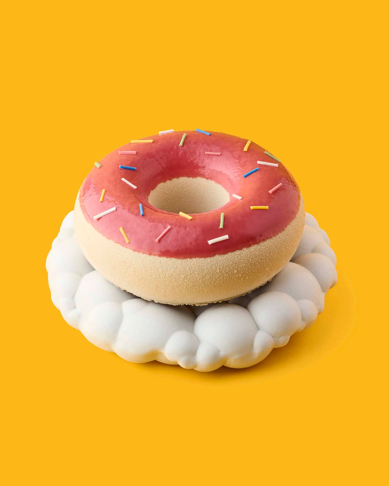 Pink glazed ring pastry with colorful sprinkles on a white cloud-shaped stand against a yellow background at GLO Pasticceria