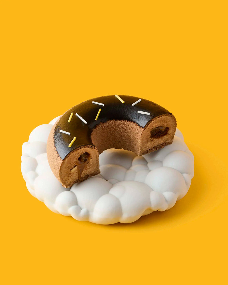 Chocolate filled donut pastry with sprinkles on a white plate against a yellow background from GLO Pasticceria
