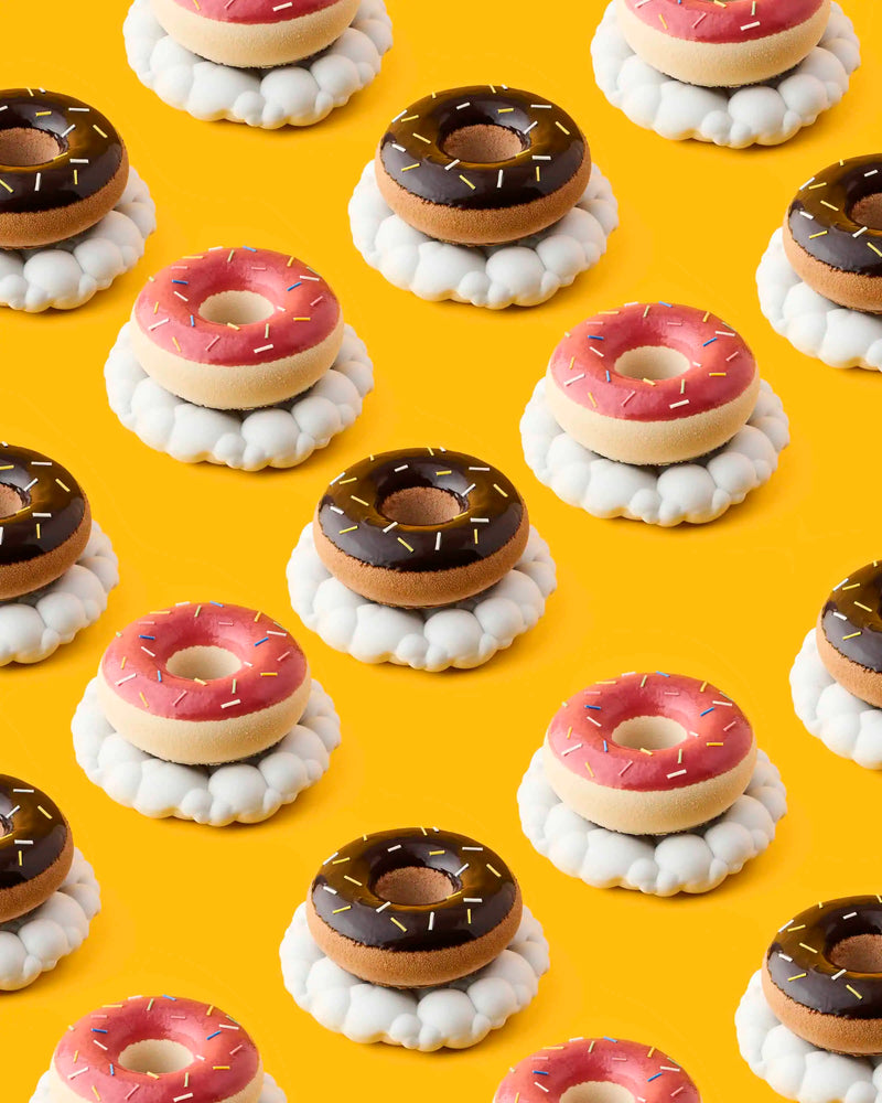 Pattern background of pink and chocolate glazed donuts with sprinkles on white cloud plates over a yellow background at GLO Pasticceria